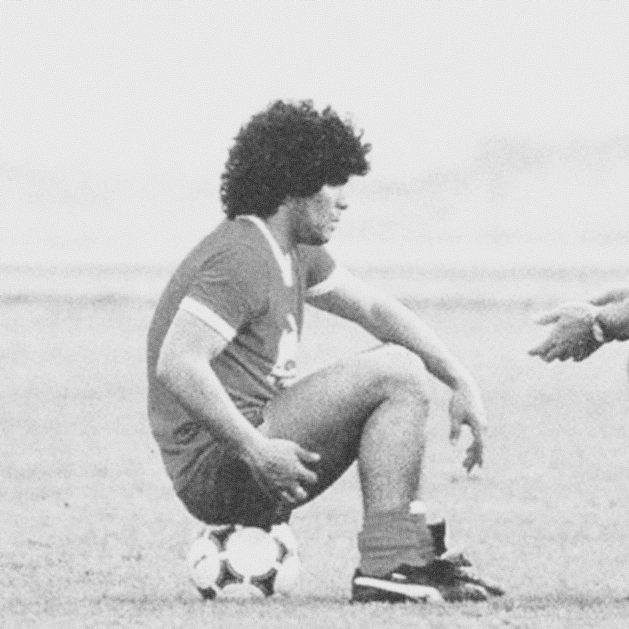 Diego Maradona sitting on football